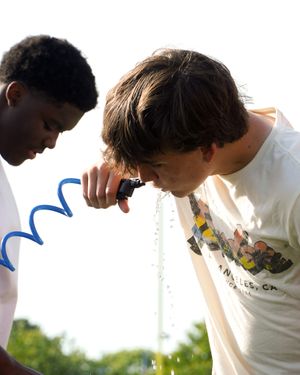 Two young athletes drinking from water fountains outdoors.