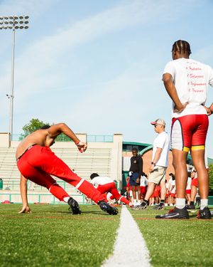 Athletes practicing drills on football field with stadium lights in background.