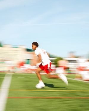 Motion blur photo of athlete running on football field in red and white uniform.