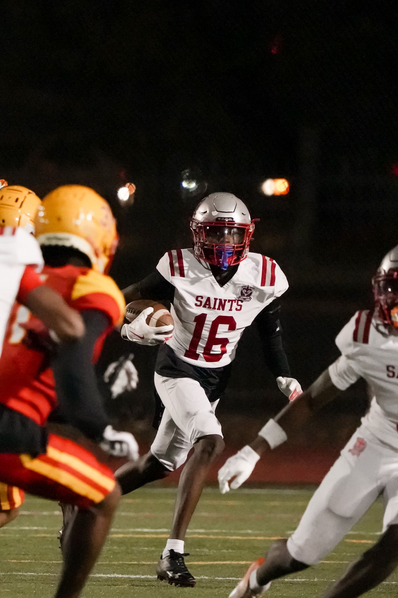 Football player in white Saints uniform carrying ball during nighttime game.