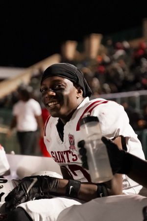 Football player in white Saints jersey smiles while sitting on sideline during game.