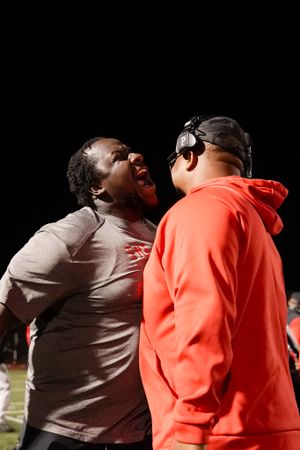 Two coaches share an animated conversation on the football field sideline.