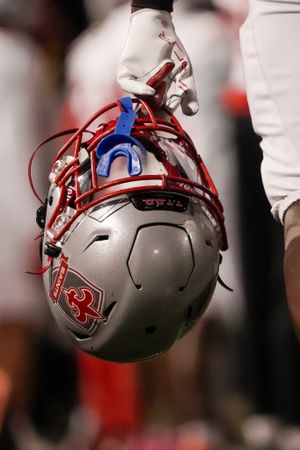 Close-up of player holding silver and red football helmet with protective face mask.