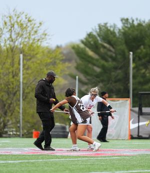 Lacrosse players and officials gather around center field during a match on an artificial turf field.
