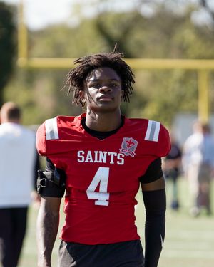 Football player wearing red Saints jersey number 4 stands on field.