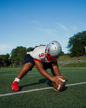 Football player in silver helmet practices snap position with ball on field.