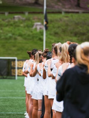 Game-ready sports team players in white uniforms gathered in line formation on a turf field during a sunny day.