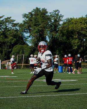Football player in white and red uniform runs with ball during outdoor game.