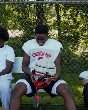 Football player on bench holds white helmet while wearing Concordia Park uniform.