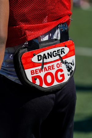 Red fanny pack with 'Danger Beware of Dog' warning sign worn over black pants.