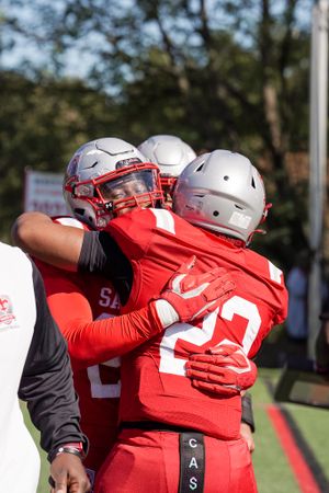 Football players embrace during game wearing red and white uniforms.