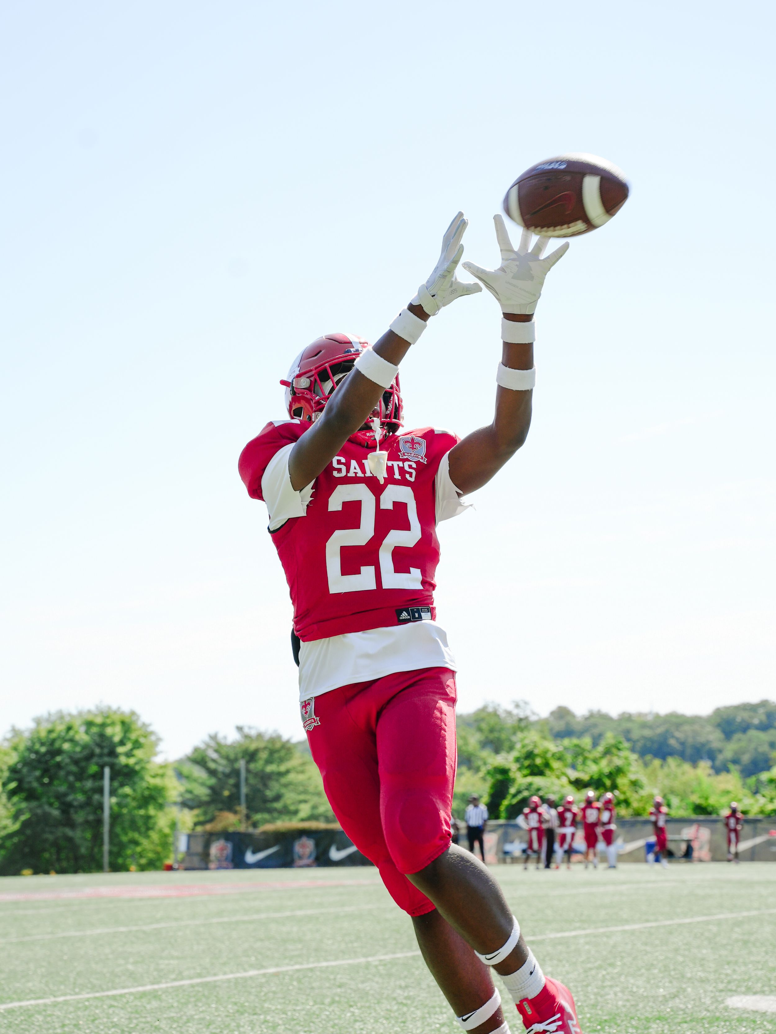 Football player in red jersey leaps high to catch a football in a sequence of athletic action shots on a grass field.