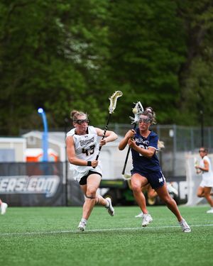 Two lacrosse players in action on a field, one in white and one in navy uniforms competing for ball possession.
