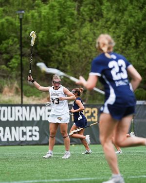 Player in white uniform raises lacrosse stick during intense tournament match on outdoor turf field.