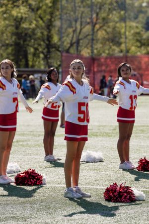 Cheerleaders in red and white uniforms perform a synchronized routine on a sunny field with pom poms.