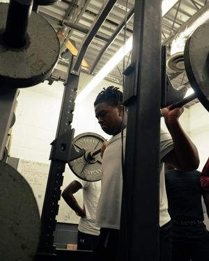 Athlete prepares for a weightlifting exercise in a gym setting with equipment in the background.
