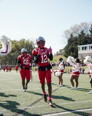 Football players in red uniforms run onto the field while cheerleaders cheer.