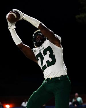 Football player in white uniform number 23 makes dramatic catch against dark background.