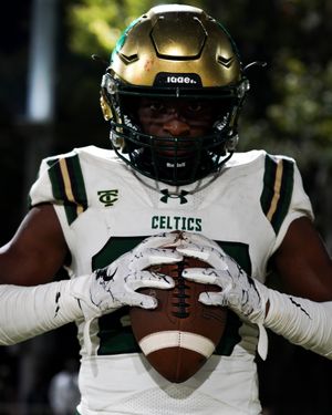 Celtic football player wearing helmet holds football against white jersey uniform.