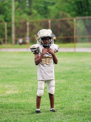 Young athlete in white jersey #6 stands ready with football on grass field during practice or game.
