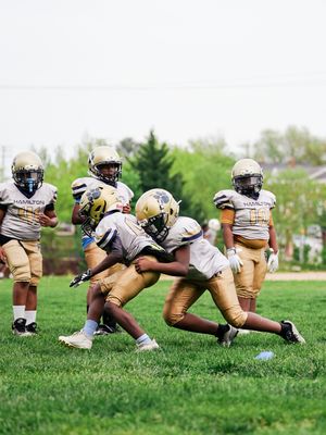 Football players in gold uniforms practice tackling drills on a grassy field during team training session.