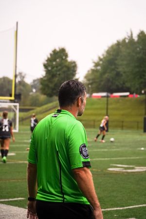 Soccer referee in bright green uniform observing match from sideline.