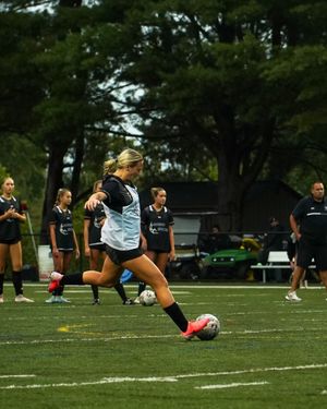 Soccer player kicking ball on athletic field surrounded by teammates.