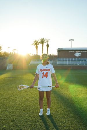 Florida Gators lacrosse player in white uniform #14 poses on field during golden hour sunset.