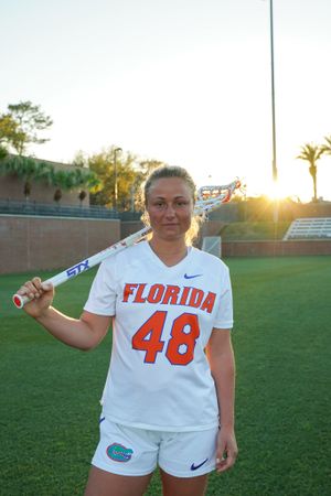 Florida Gators lacrosse player in uniform #48 poses with stick on field at sunset.