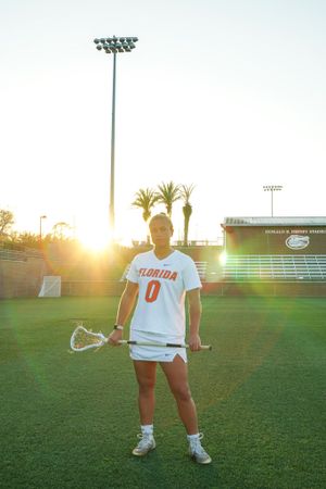 Athlete in Florida Gators #0 jersey stands on lacrosse field during sunset.