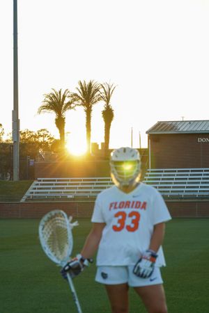 Silhouetted lacrosse player in Florida #33 uniform against palm trees and setting sun.