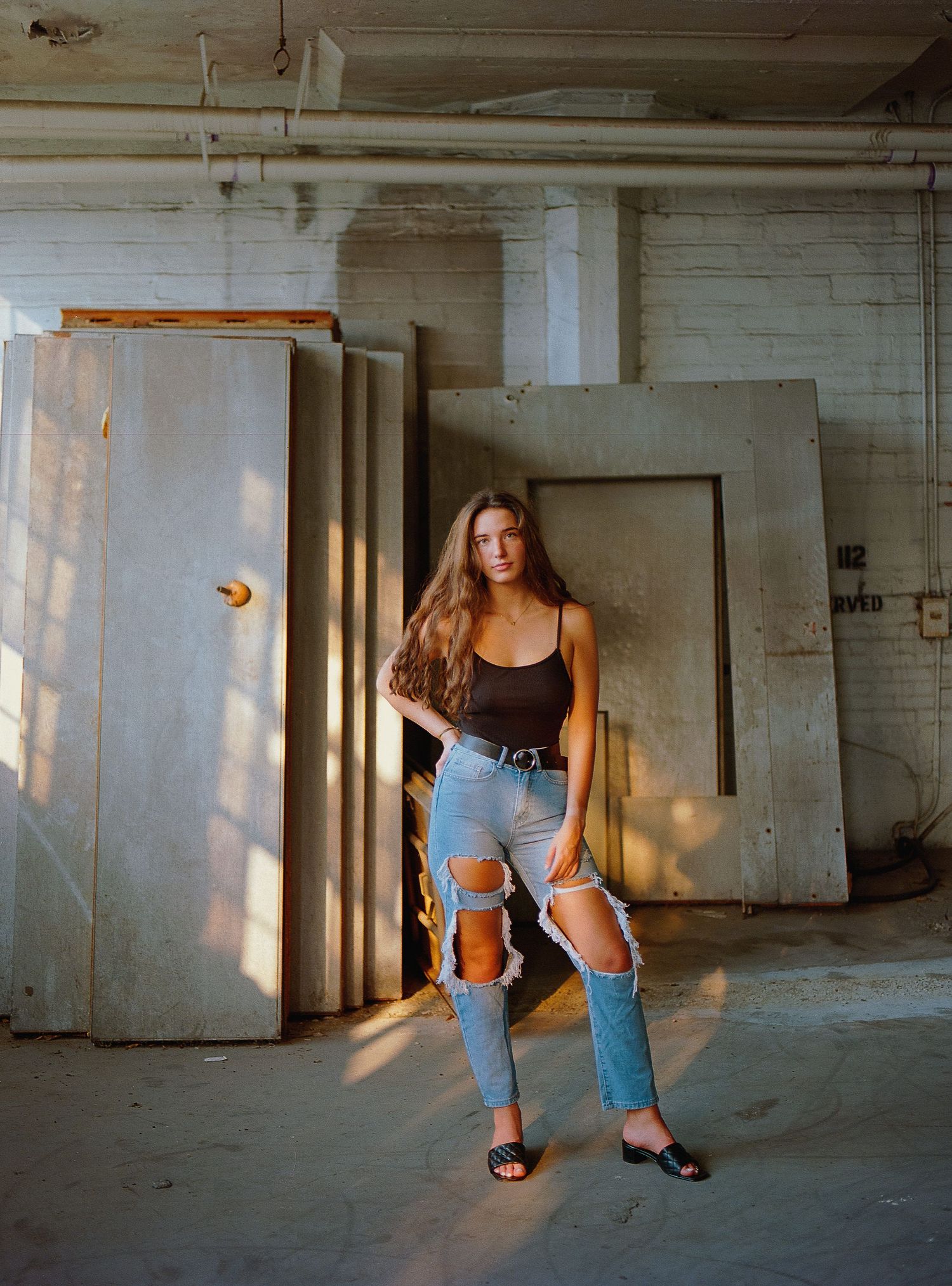 Urban fashion portrait in industrial setting with distressed jeans and black top.
