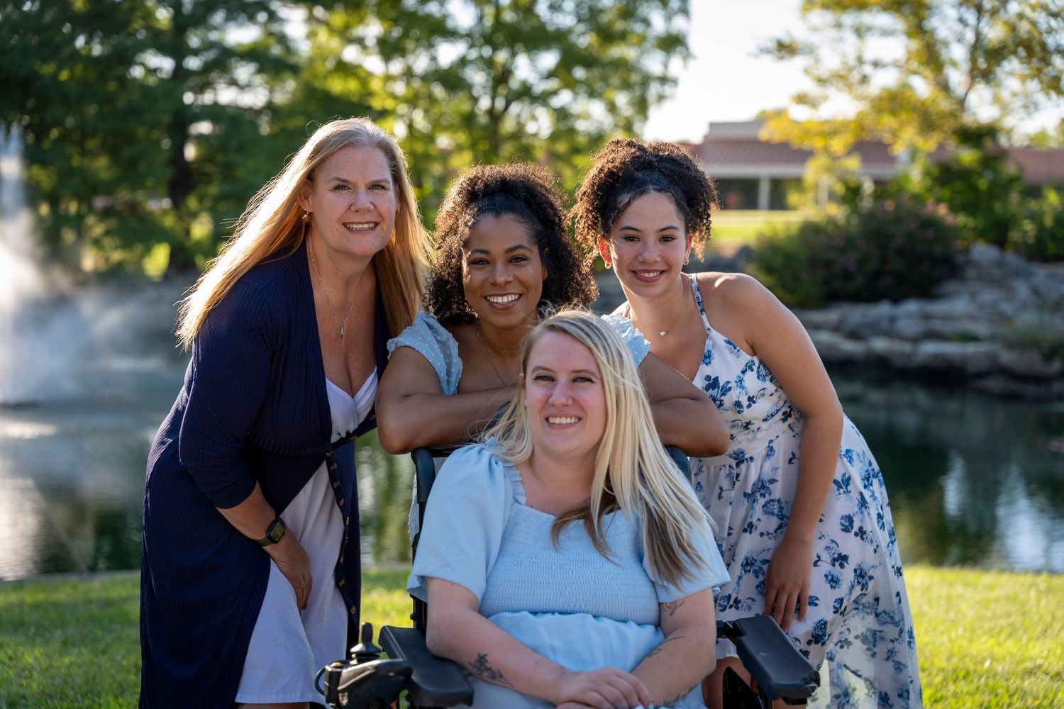 Friends gather close together for an outdoor photo with a pond and trees in the background.