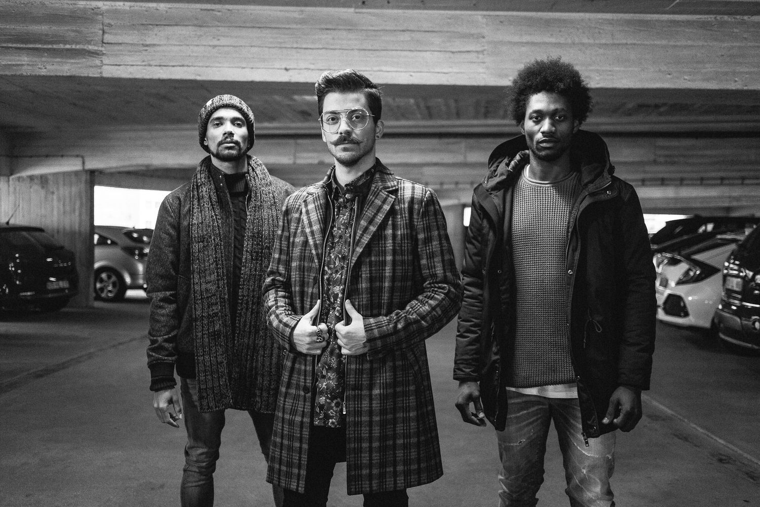 Three people wearing winter coats stand together in a parking garage in black and white photography.