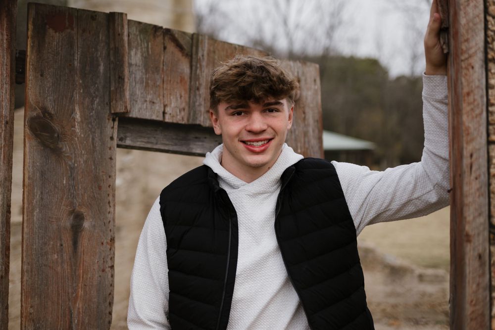 Winter portrait showing someone in white hoodie and black vest by wooden door.