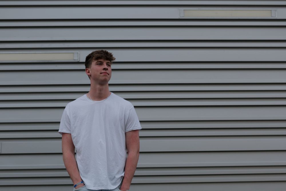 Minimalist portrait against gray siding wall wearing white t-shirt.