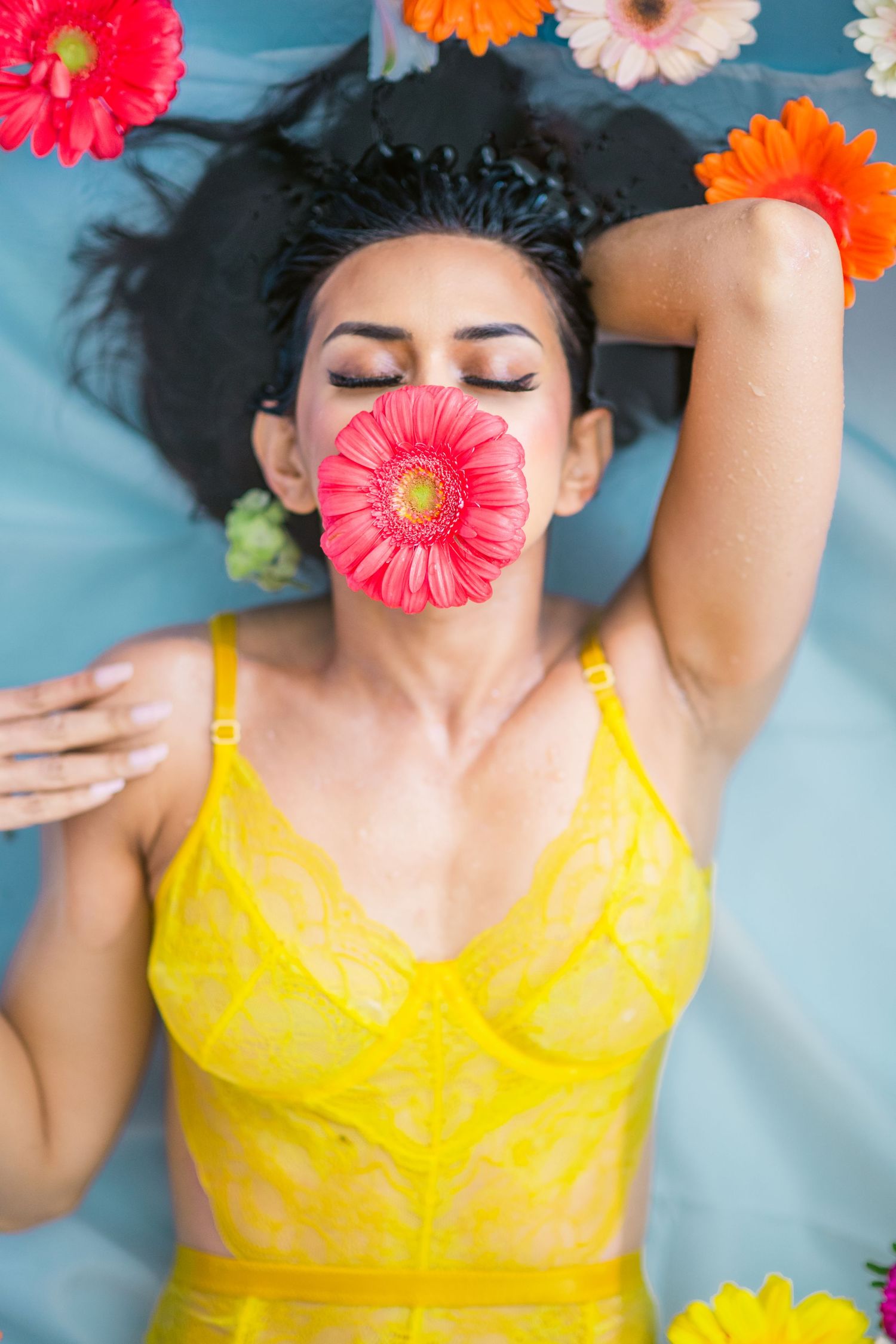Artistic portrait in yellow swimwear with pink gerbera daisy against blue water background.