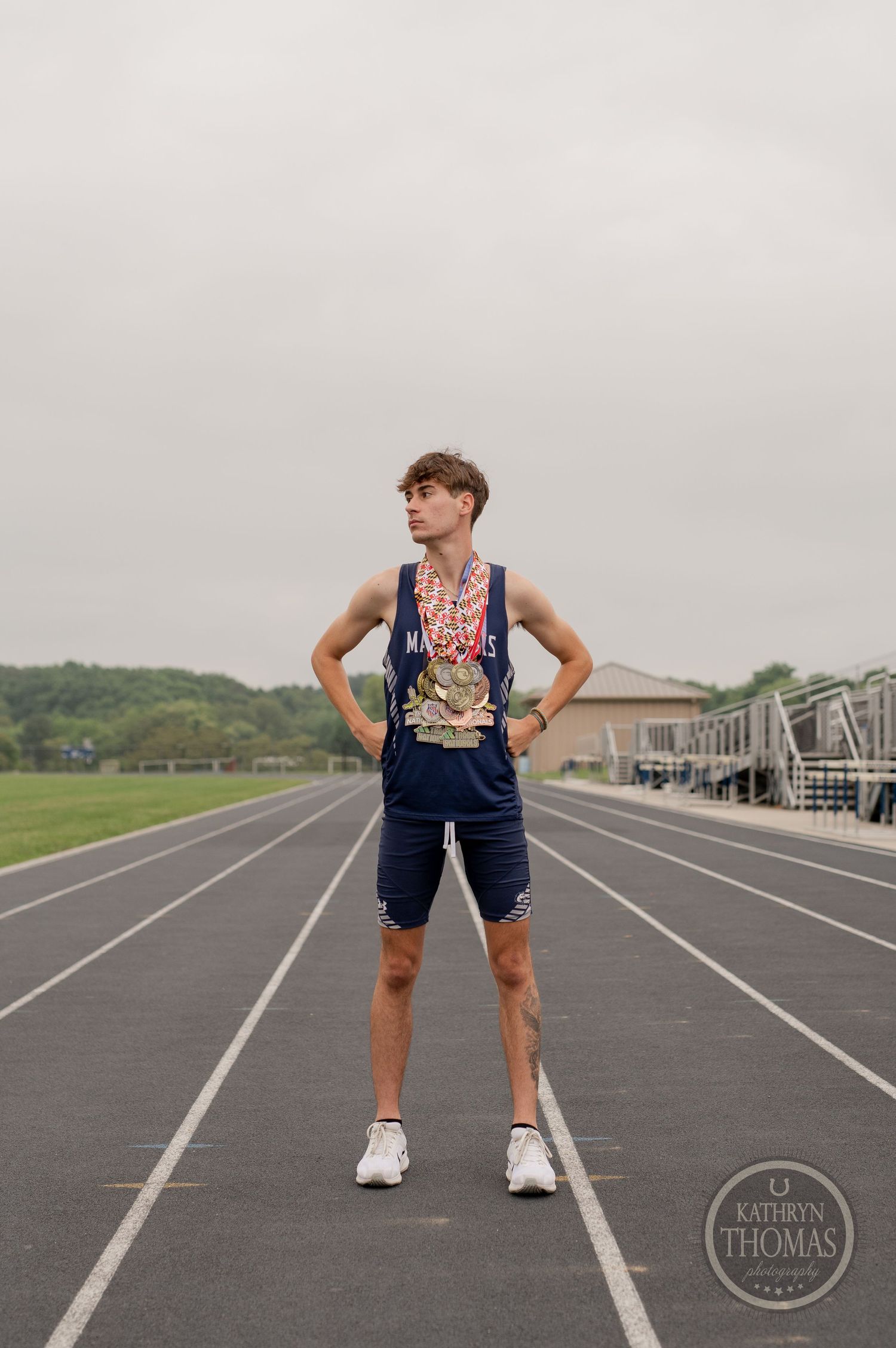 An athlete poses confidently on a running track wearing medals and navy athletic wear.