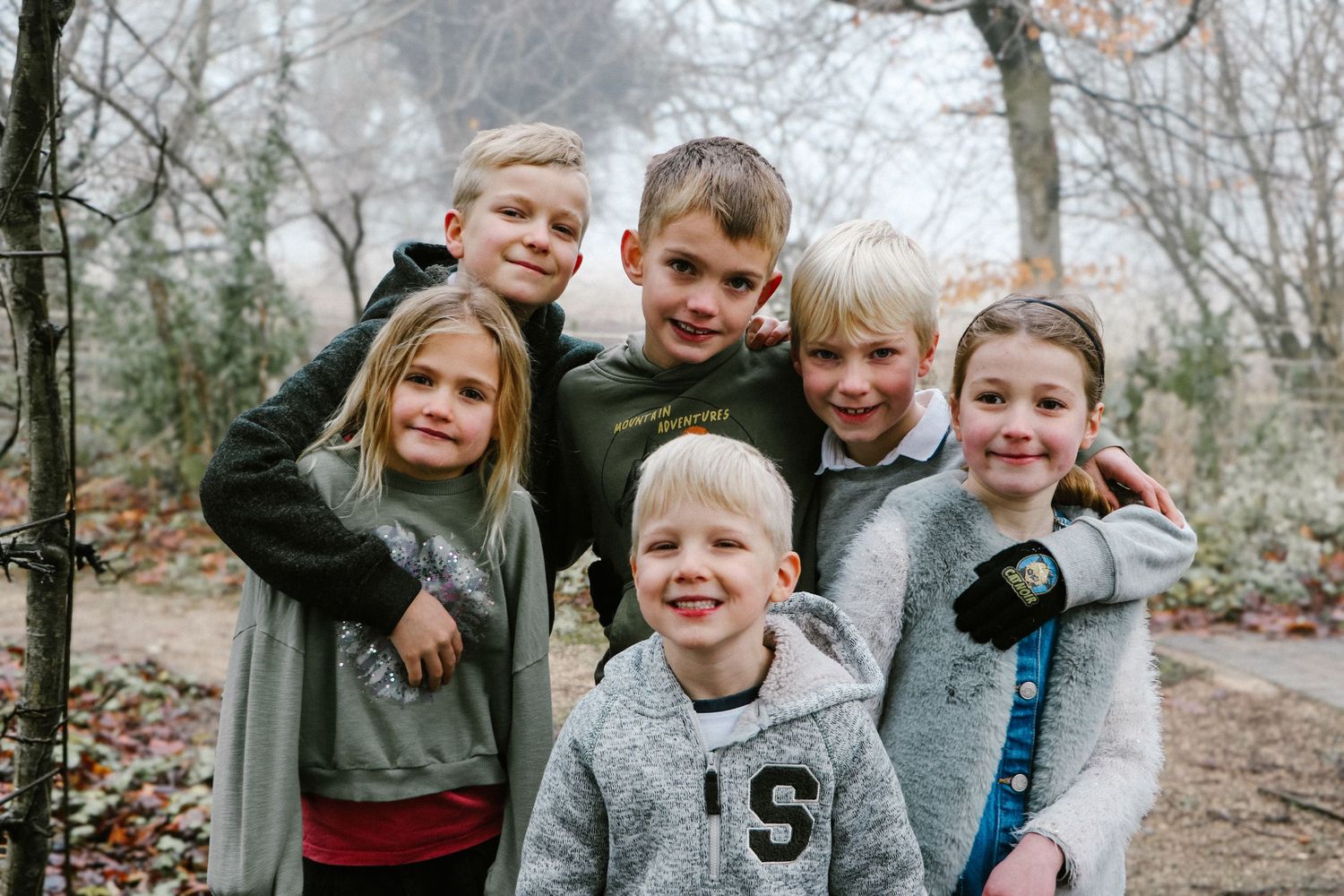 A group of children huddle together smiling on a wooded path during autumn.
