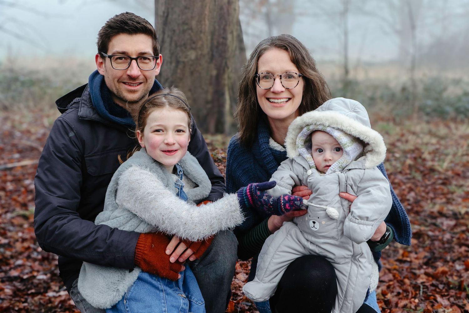 A family enjoys quality time together on fallen autumn leaves in a park during a cool fall day.