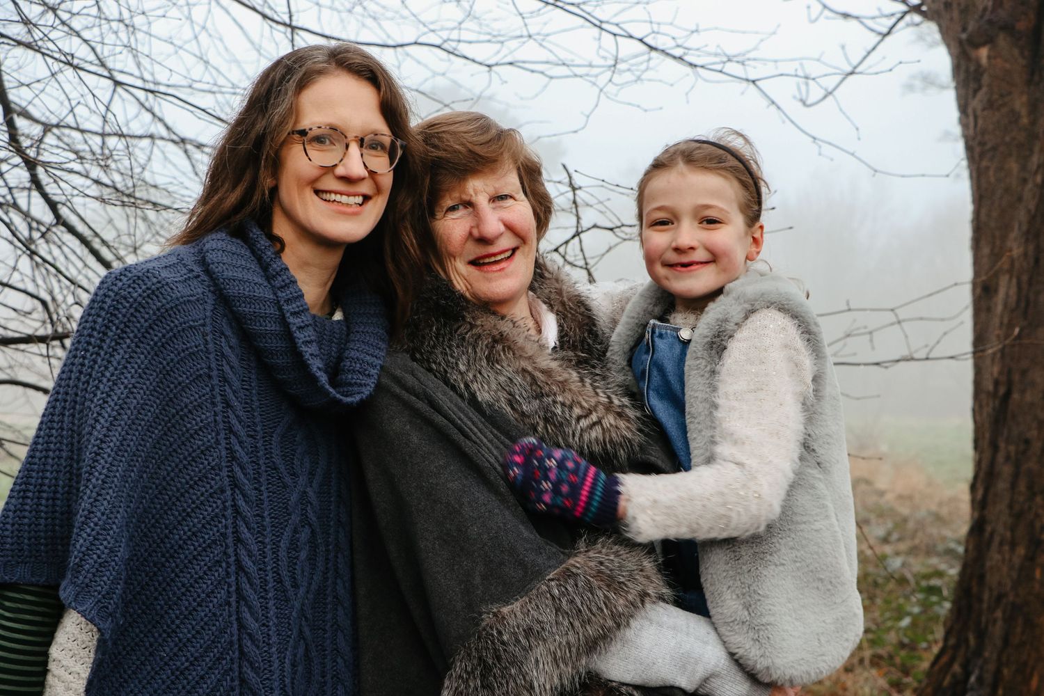Three people wearing cozy winter sweaters smile together outdoors on a foggy autumn day.