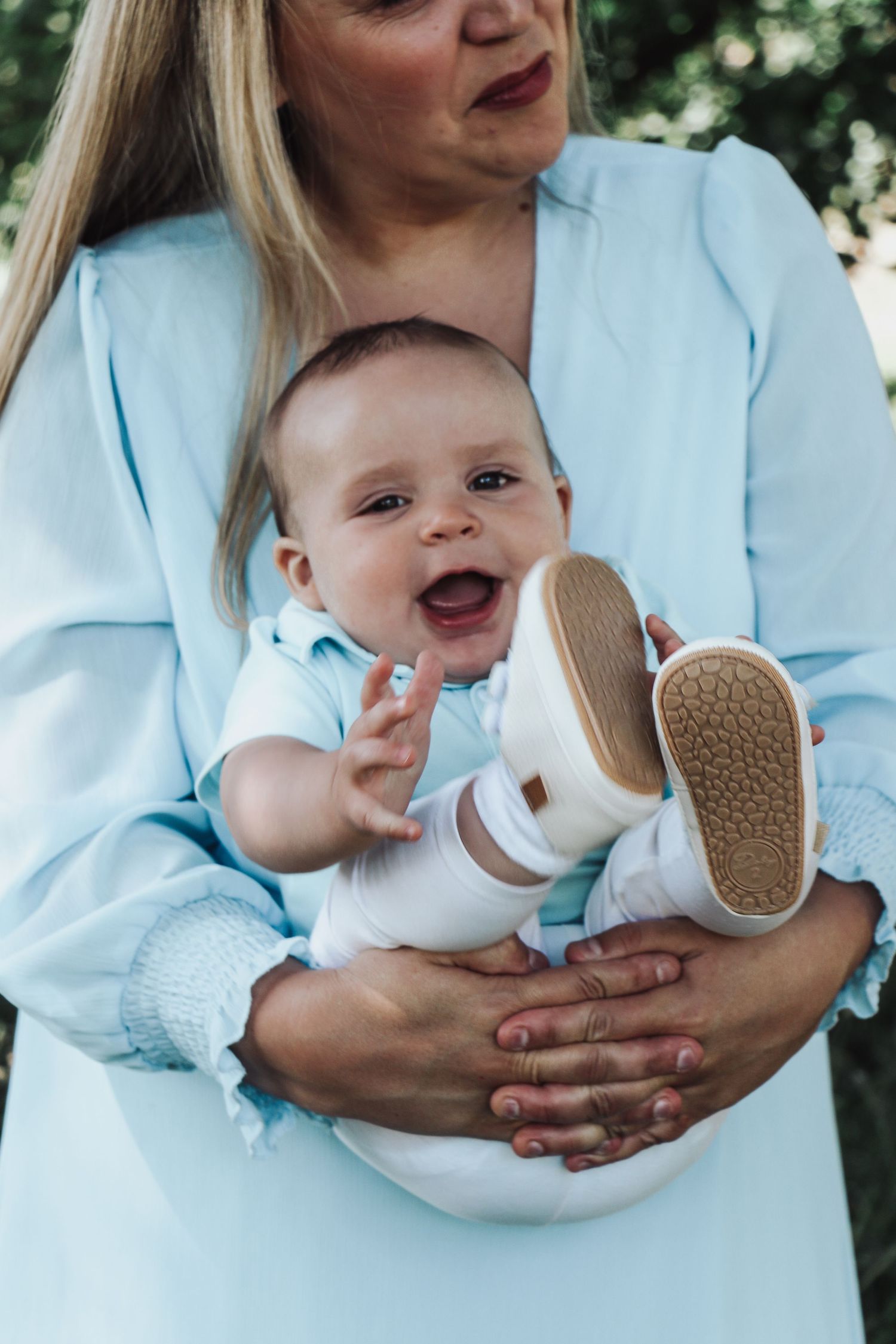 Happy baby in white outfit being held while showing excitement.