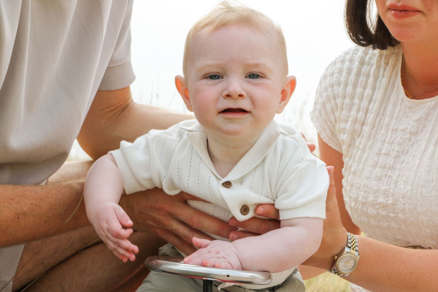A baby sits supported while playing with a toy car outdoors.