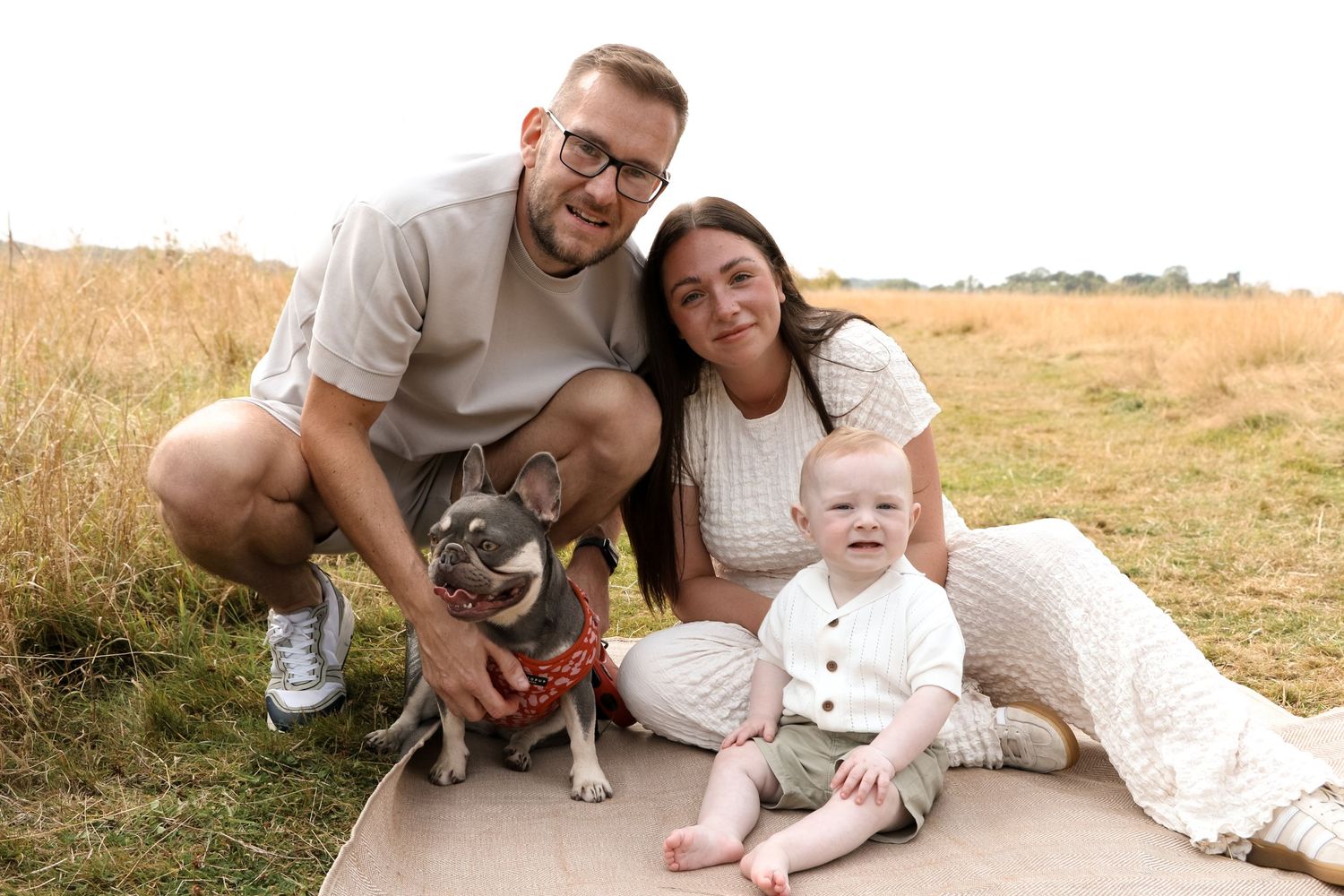 A family and their Boston Terrier dog pose together on a path in a golden wheat field.