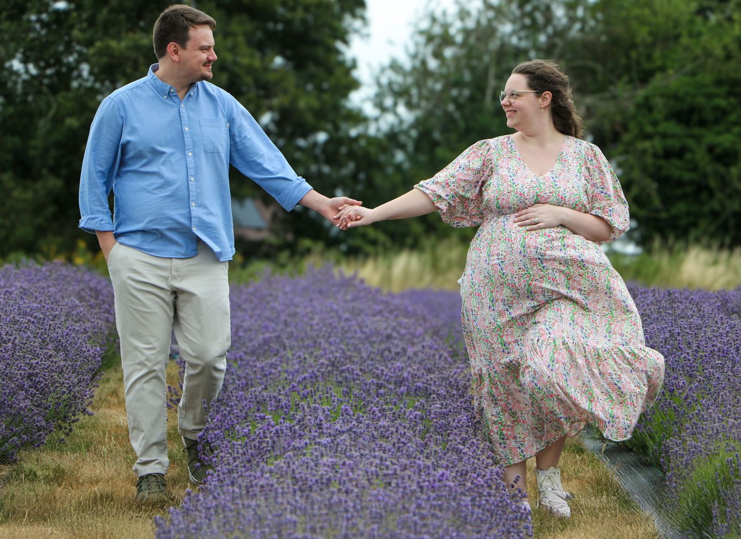 A couple holds hands while walking through a blooming lavender field on a summer day.