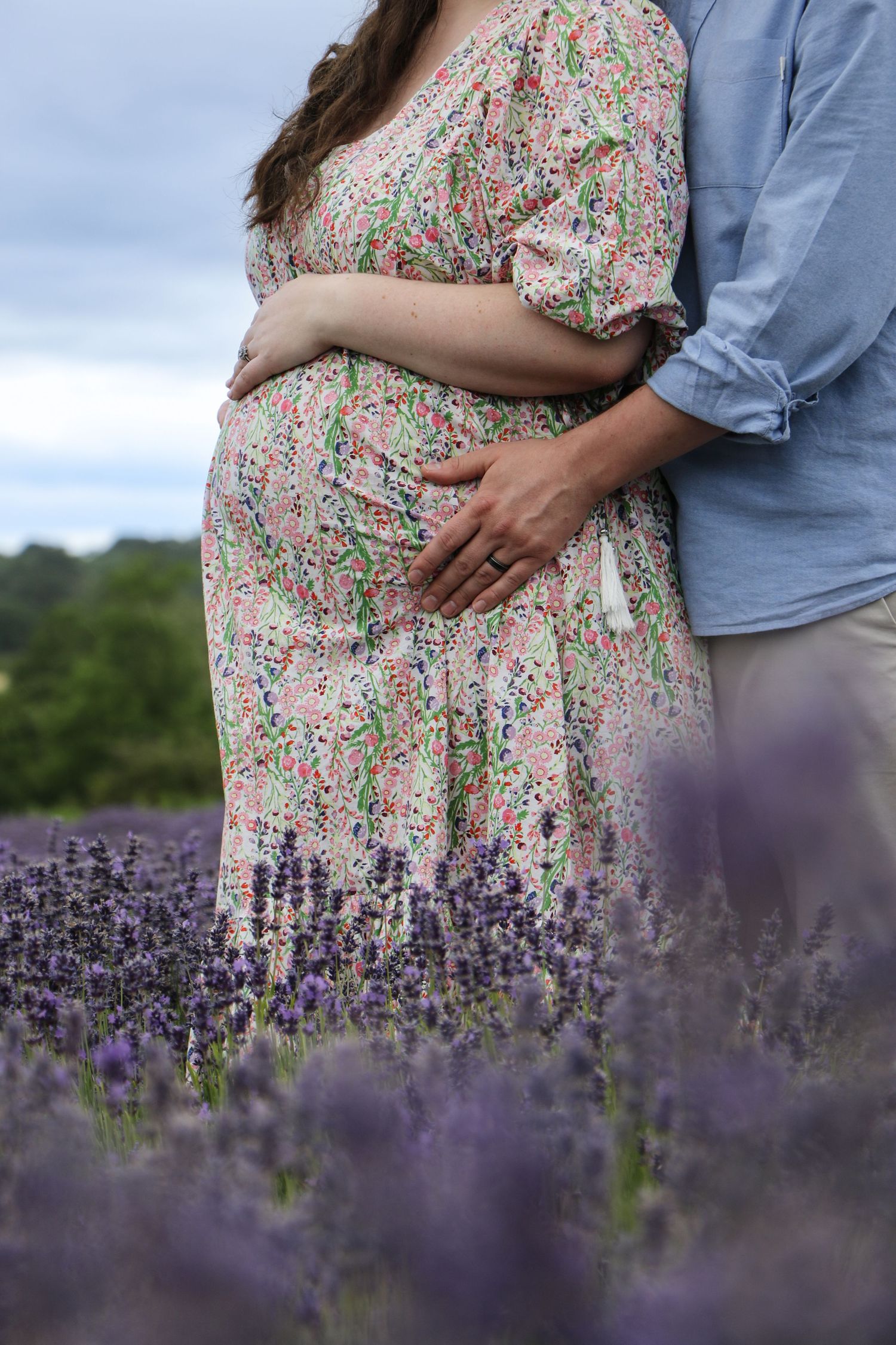 Romantic couple embraces in a blooming lavender field with soft lighting and floral dress details.