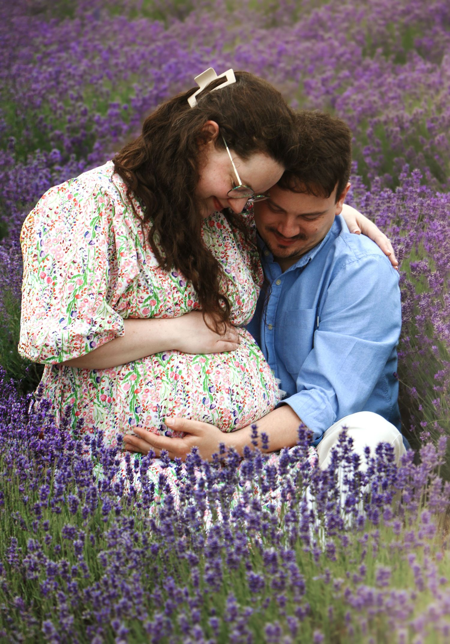 A couple shares an intimate moment sitting together in a blooming purple lavender field on a sunny day.