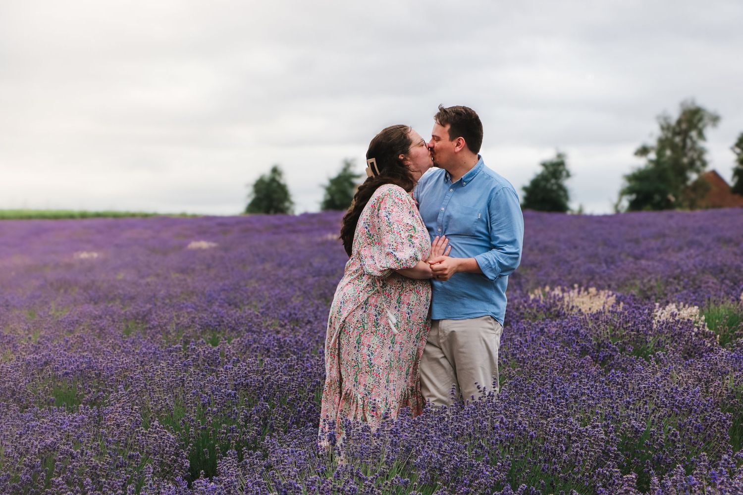 A couple shares a romantic moment in a blooming purple lavender field on a cloudy summer evening.