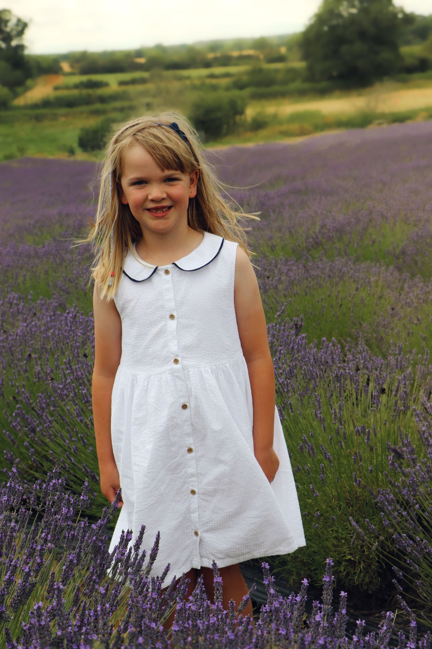 A white dress flows in the breeze against a vibrant purple lavender field on a sunny summer day.