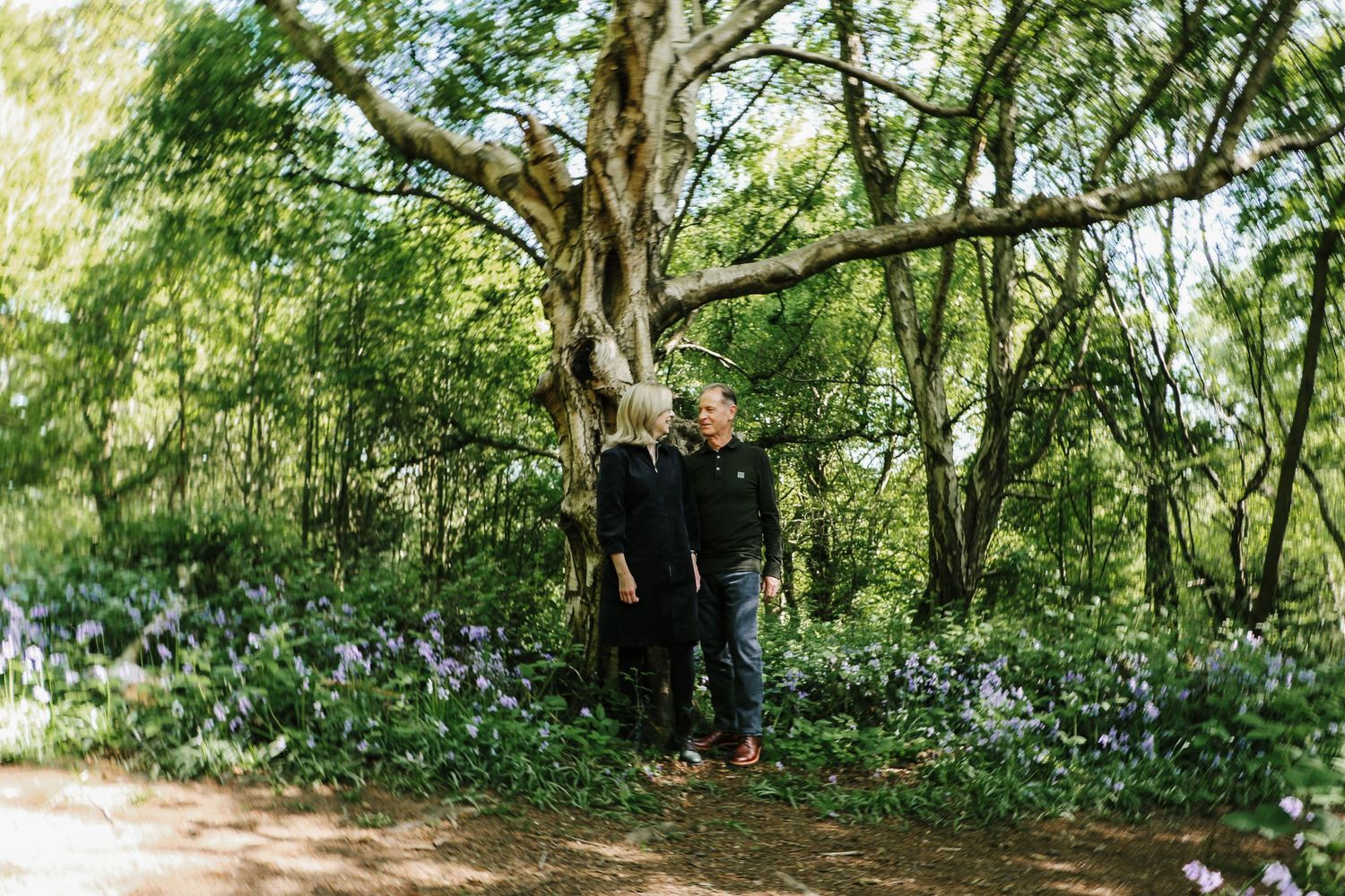 A lush wooded trail with sunlight filtering through green trees and dense foliage along the path.